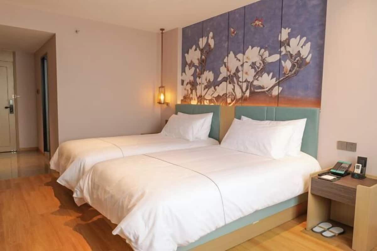 A hotel room with a bed, a nightstand, a wall-mounted lamp, and a painting.