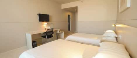 A hotel room with two beds, a desk with a chair, a TV, and a wall-mounted light.