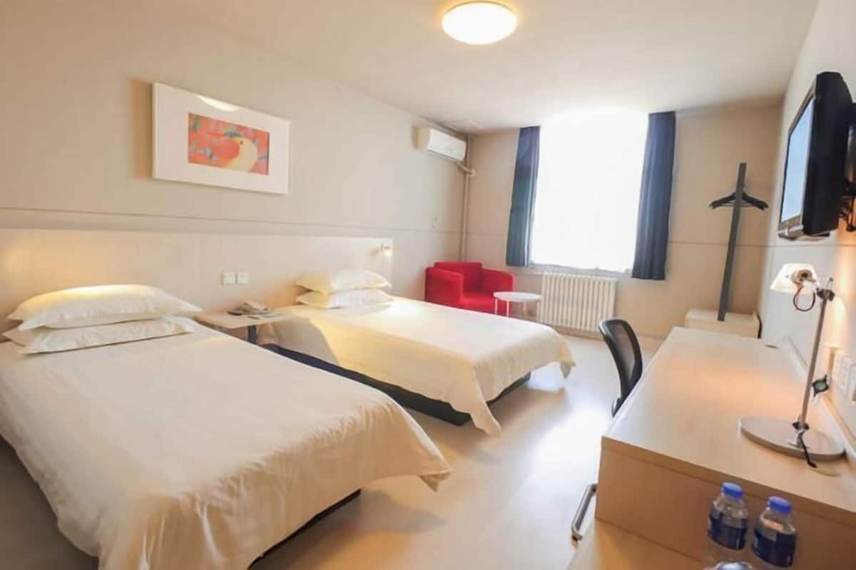 A hotel room with two beds, a desk with a chair, a TV, and a window with curtains.