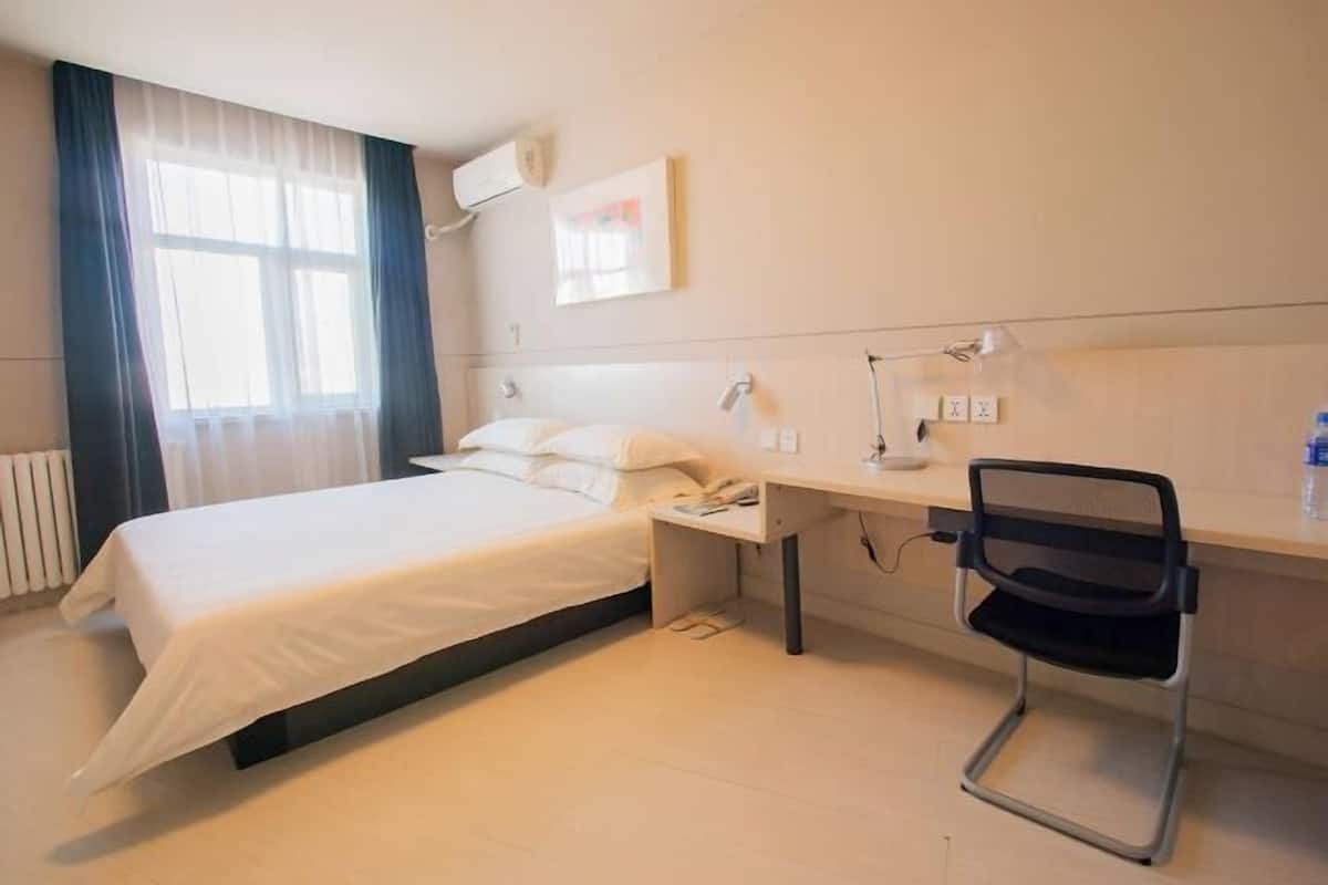 A hotel room with a bed, desk, chair, and a window with curtains.