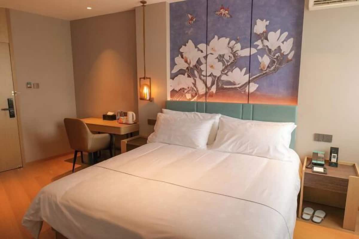 A hotel room with a bed, a desk, a chair, a nightstand, and a wall-mounted artwork.