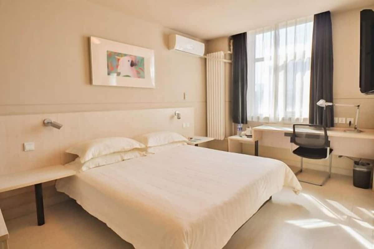 A hotel room with a large bed, a desk, a chair, and a window with curtains.