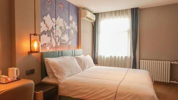 Habitació d'hotel amb un llit, una taula, una cadira, una làmpada penjada a la paret i una finestra amb cortines.