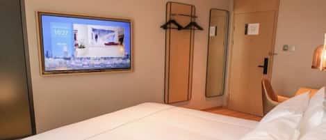 A hotel room with a bed, a TV mounted on the wall, a mirror, and a chair.