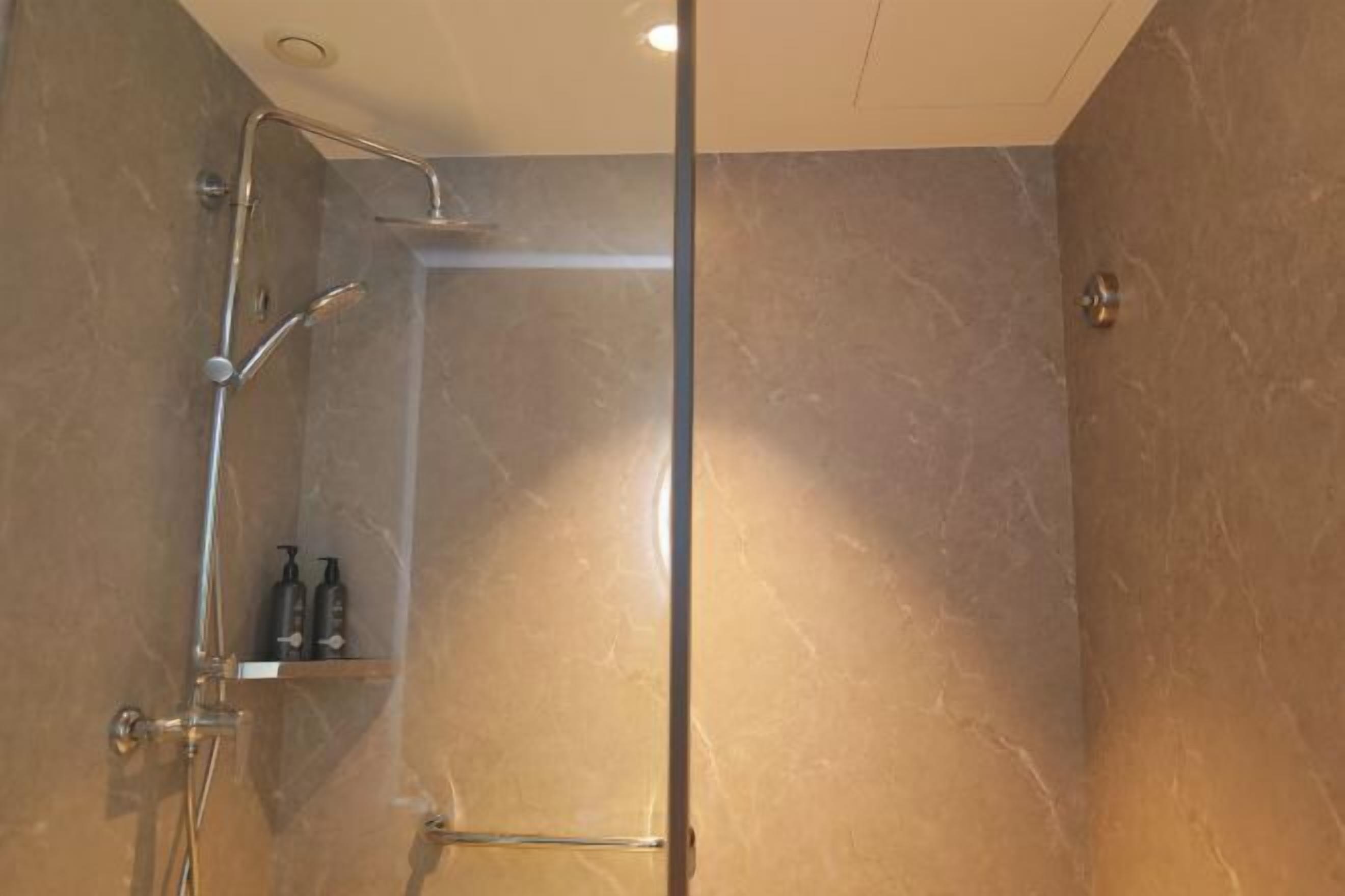 A modern bathroom with a glass-enclosed shower, marble walls, and a shelf with toiletries.