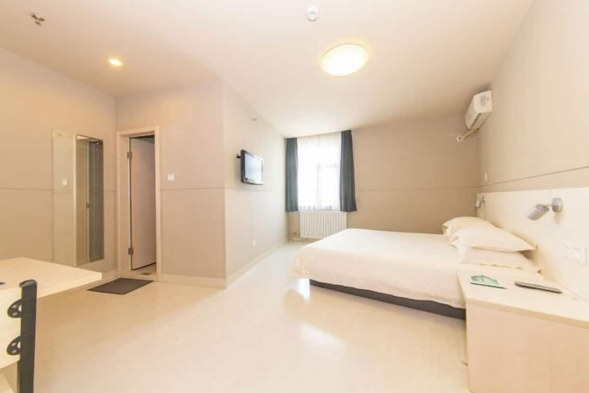 A hotel room with a bed, bedside table, and a television on the wall.