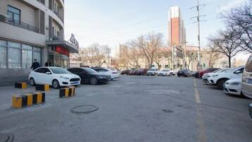 Un estacionamiento con varios autos, un edificio con un letrero y un edificio alto al fondo.