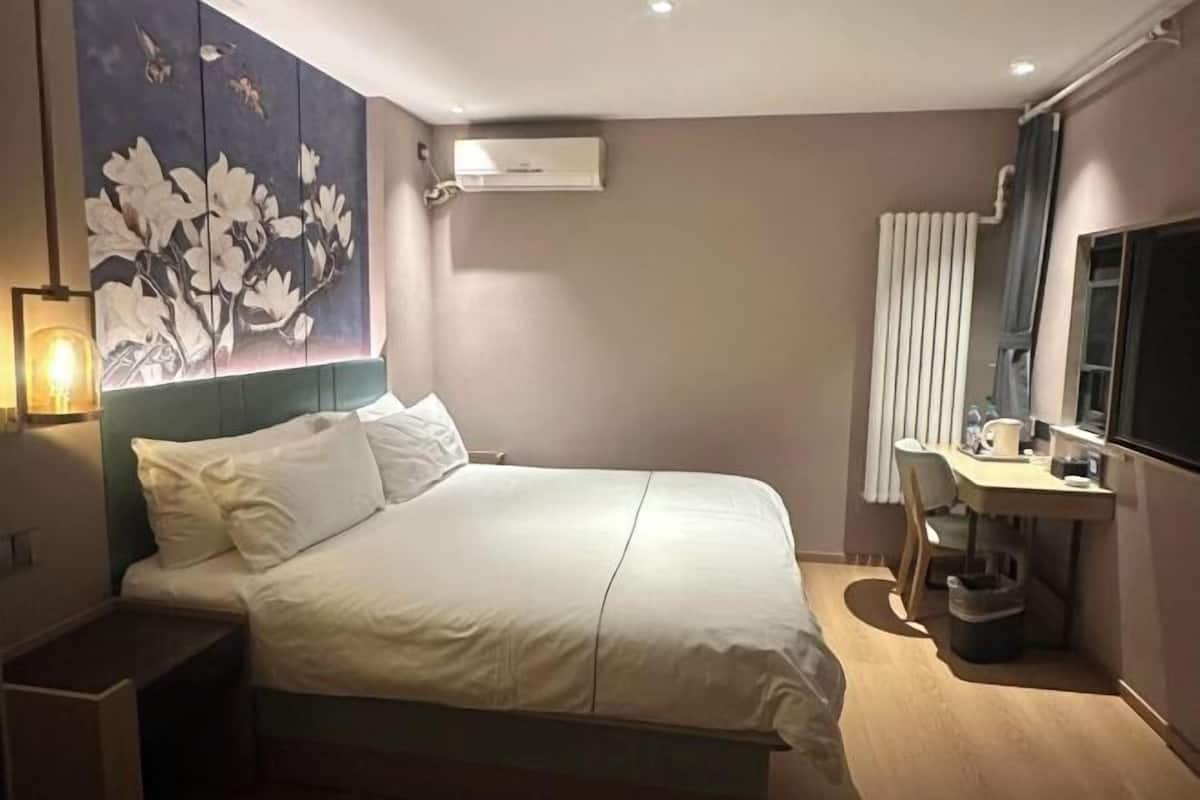 A modern hotel room with a large bed, a desk, and a wall-mounted air conditioner.