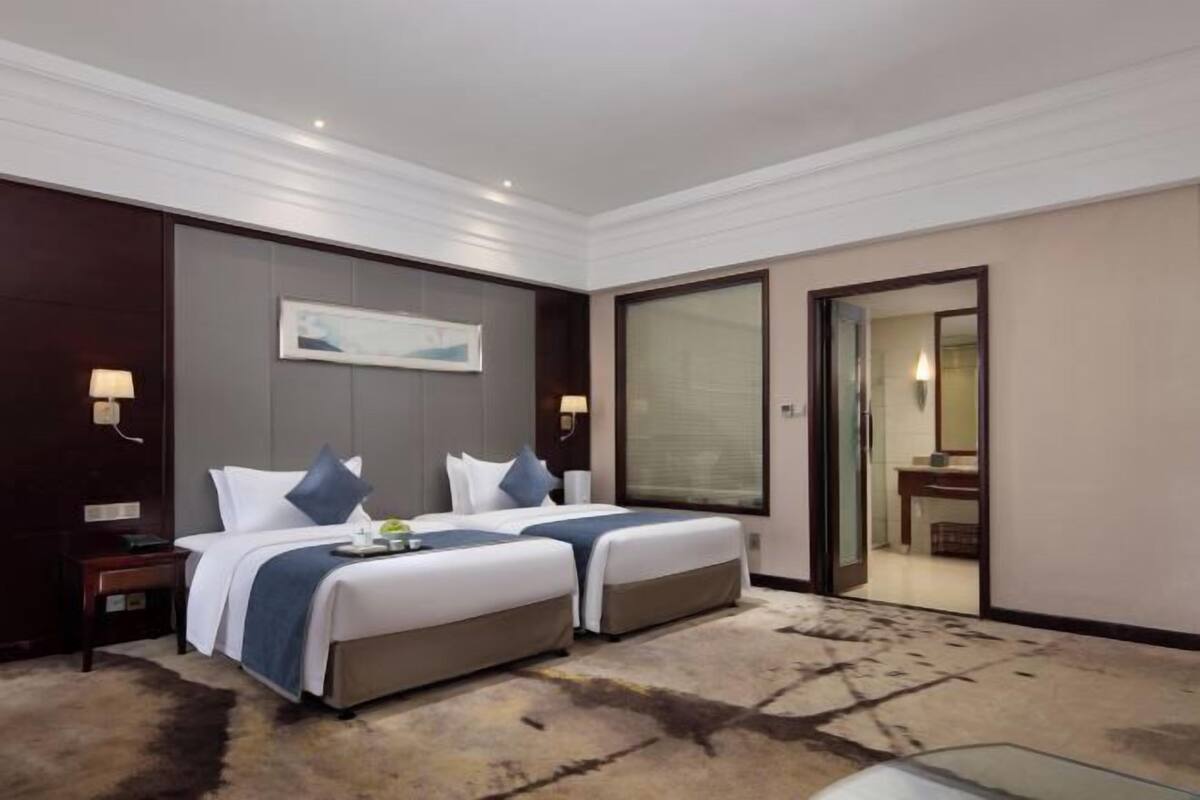 Habitación de hotel con dos camas, un espejo grande, suelo alfombrado y vista al baño.