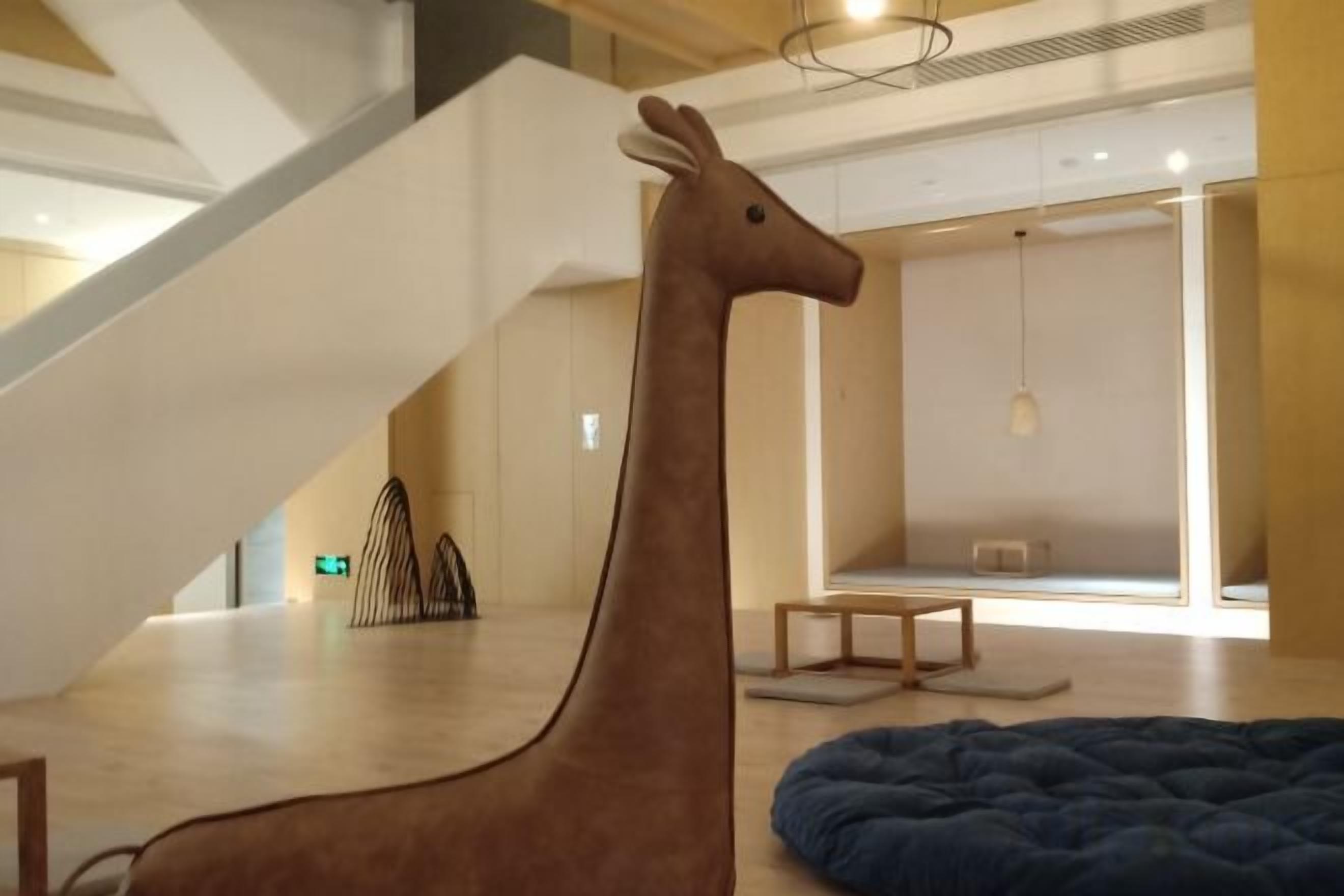 A giraffe sculpture in a modern interior space with a staircase and a blue circular seating area.