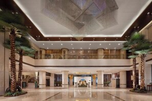Um hall amplo com pé direito alto, palmeiras e uma área decorativa central.