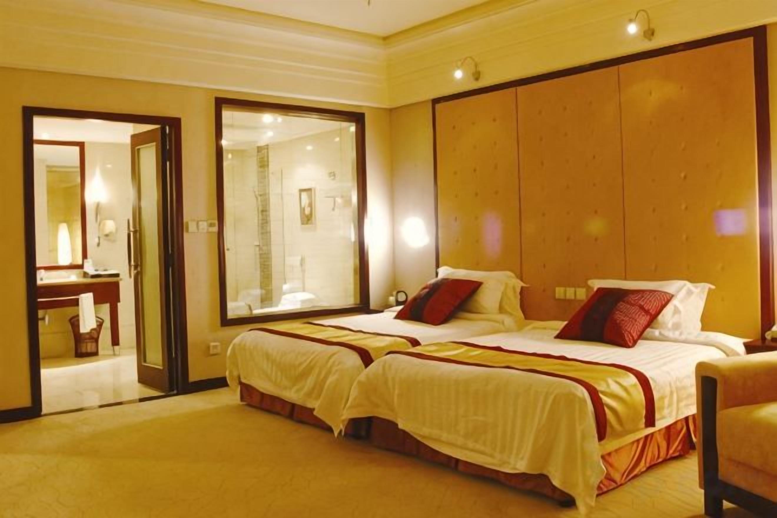 Habitación de hotel con dos camas, zona de estar, baño y un espejo grande.