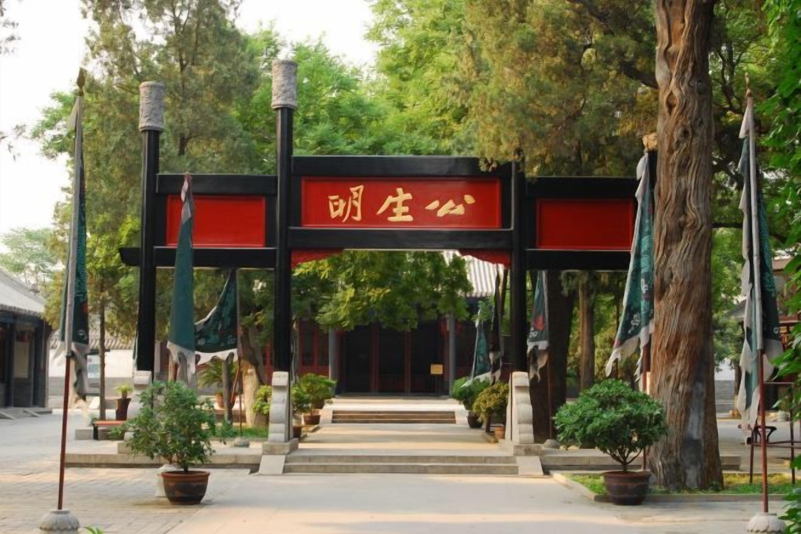 Una puerta tradicional china con un letrero rojo, rodeada de plantas en macetas y árboles.