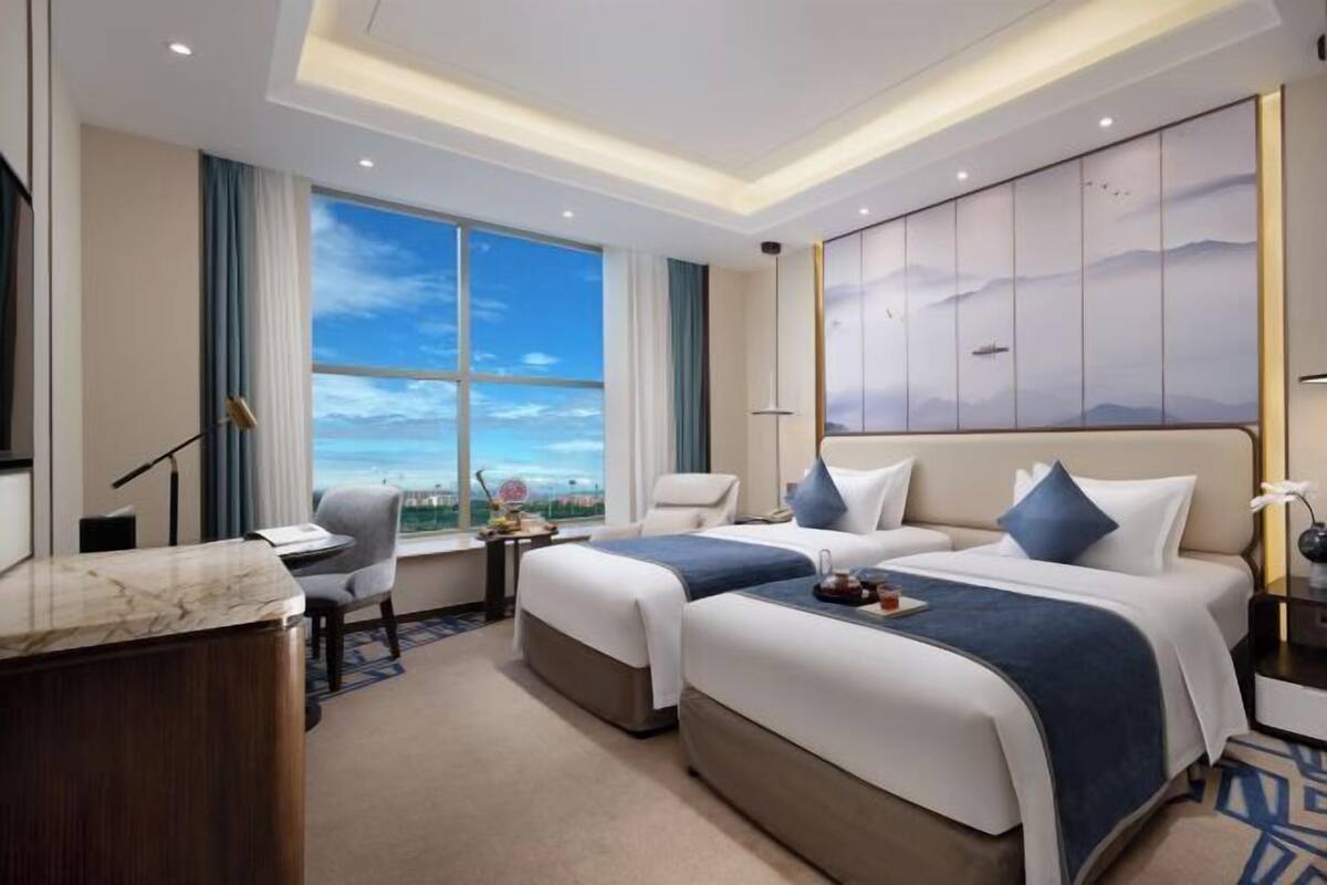 Habitación de hotel con dos camas, un escritorio, una silla, un ventanal con vistas y un televisor montado en la pared.