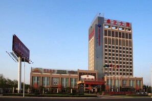 A hotel with a prominent entrance, a tall building in the background, and a clear sky. - Zhuozheng International Hotel (Baoding)