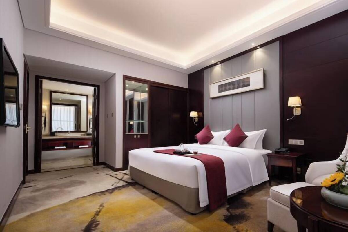 Una habitación de hotel con una cama grande, una mesita de noche, una lámpara y un espejo.
