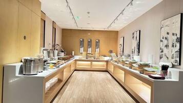 A modern hotel lobby with a central reception desk, a long counter with various amenities, and a wooden floor.