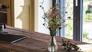 Ein Holztisch mit Blumen in einer Vase, eine Hängelampe und Blick auf Grün ins Freie.