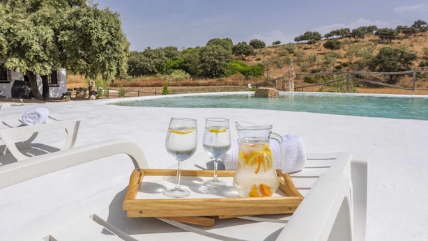 A poolside setting with a tray of drinks and a glass pitcher, overlooking a pool and a hillside with trees. - El Ventorrillo Cottage, in Morón de la Frontera (Moron De La Frontera)