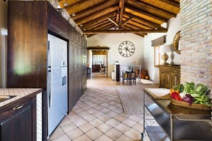 A kitchen with dark wooden cabinets, a tiled floor, a clock on the wall, and a basket of fresh vegetables on the counter. - Villa Granvia - Private villa with pool in Sicily (Trecastagni)