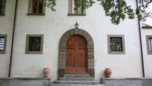 Un edifici amb una gran porta doble de fusta, una escala de passos de formigó que hi convergeix i dos testos de terracota a cada costat.