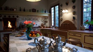 Zona de menjador amb una llar de foc, un plat de fruita i una taula posta amb coberts i un ram de flors.