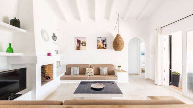 A modern living room with a sofa, coffee table, and TV. There are shelves with decorative items and a hanging light fixture. - Binire · Villa BiniRe ❤️ private pool ❤️ Free AC/Wifi (Binibequer)