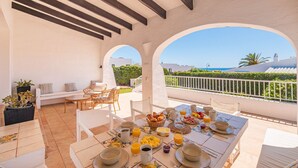 A sunlit dining area with a table set for breakfast, outdoor seating, and a view of the sea. - Binire · Villa BiniRe ❤️ private pool ❤️ Free AC/Wifi (Binibequer)