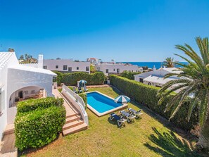 A residential area with a swimming pool, lounge chairs, and a view of the sea.