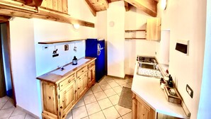 Una cocina con armarios de madera, un refrigerador azul, una estufa a gas y piso de baldosas.