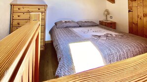 Un dormitorio con techo de madera, una cama con ropa de cama estampada, un aparador y una mesita de noche con lámpara.