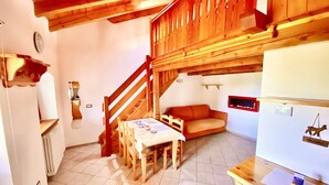 Una habitación acogedora con una escalera de madera, un sofá, una mesa de comedor con sillas y un refrigerador.