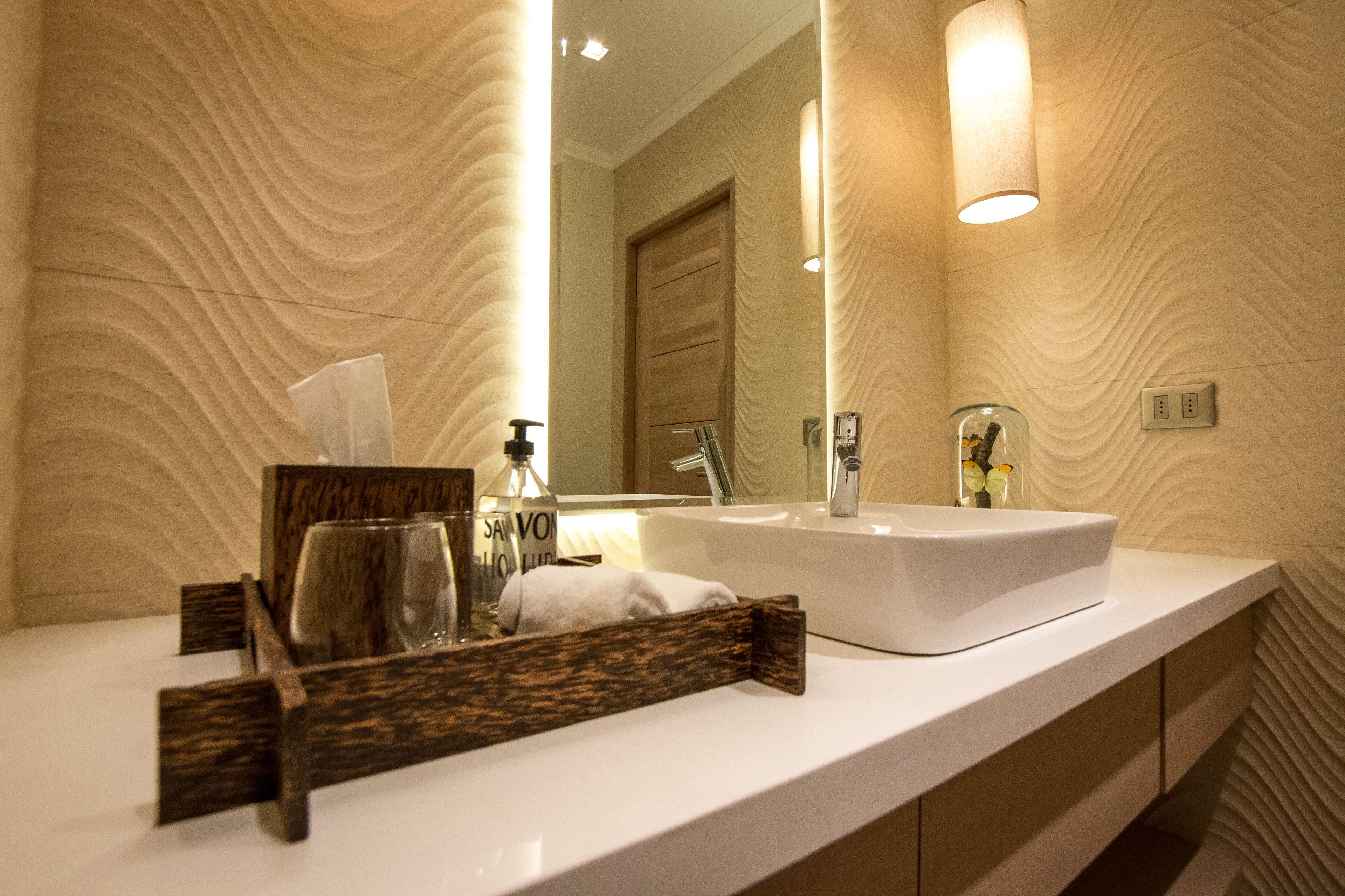 Une salle de bain moderne avec un lavabo blanc, un plateau en bois, un verre et un flacon de savon pour les mains.