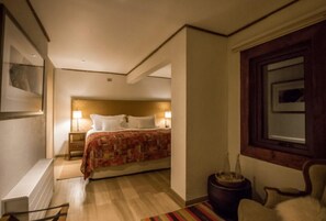 Una habitación de hotel con cama, lámparas de noche, una silla, una mesita y un ventanal.