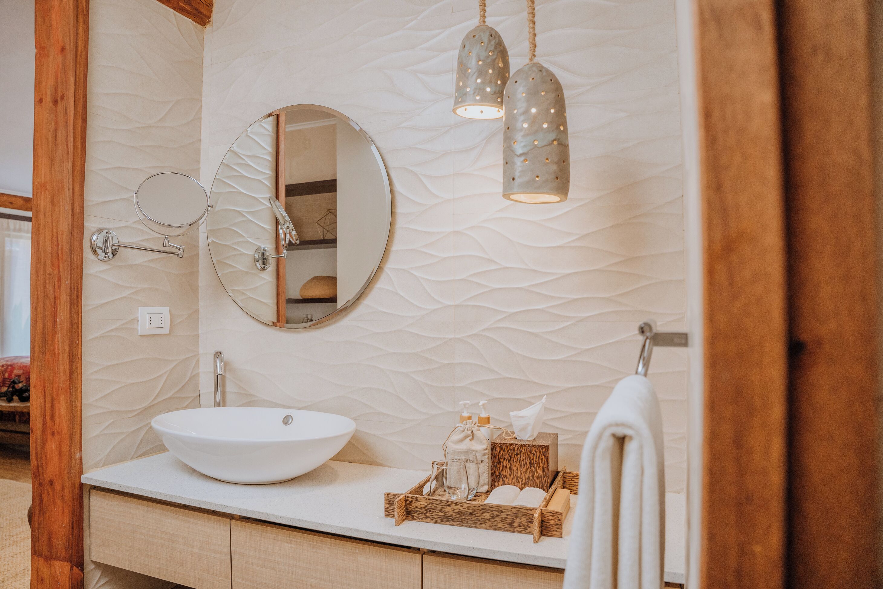 A bathroom with a round mirror, a white sink, and a wooden vanity.