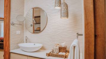 A bathroom with a round mirror, a white sink, and a wooden vanity.