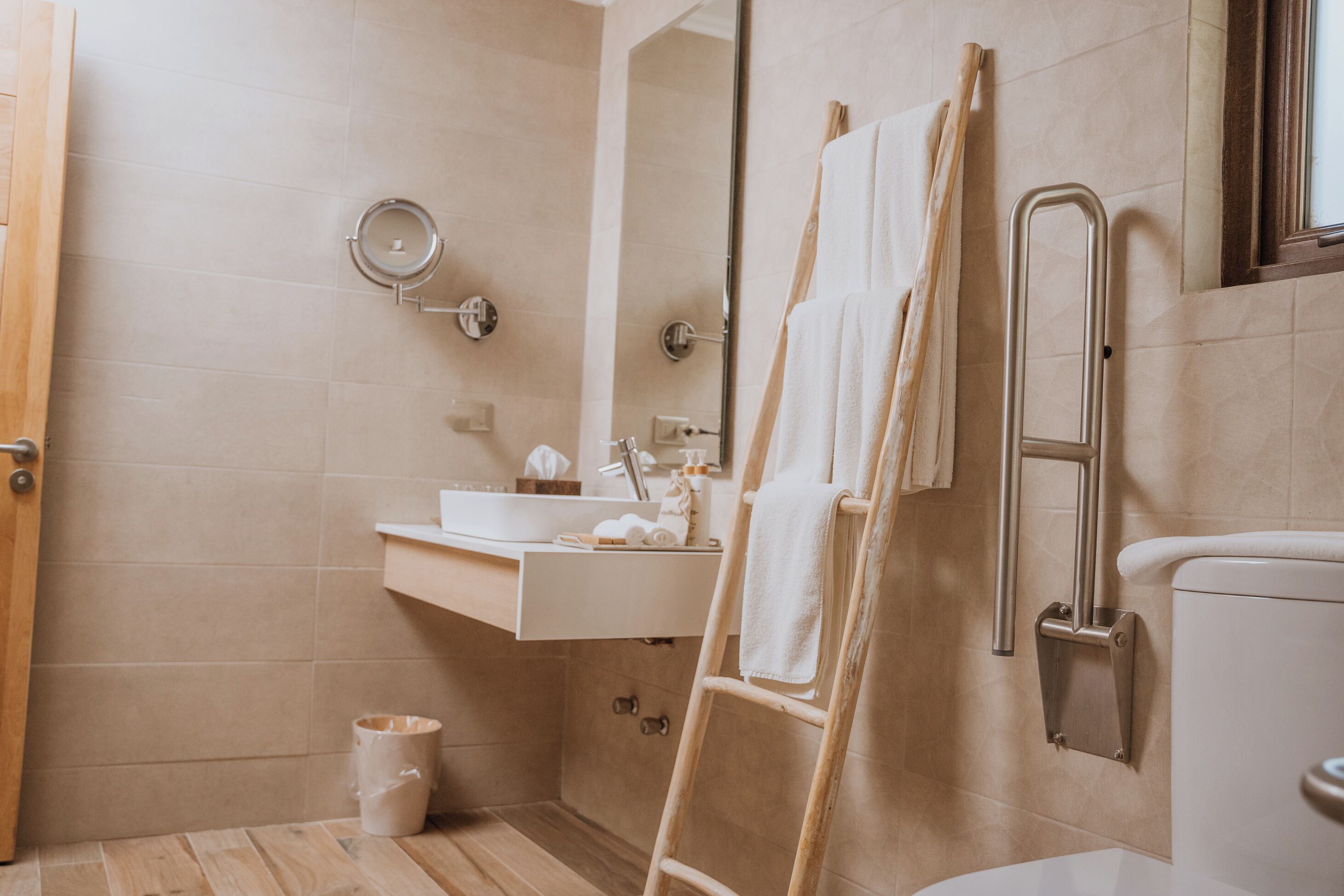 Un baño con suelo de madera, lavamanos blanco, espejo y retrete.