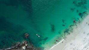 Vista aerea di una spiaggia con acque cristalline turchesi, una barca e un litorale roccioso.