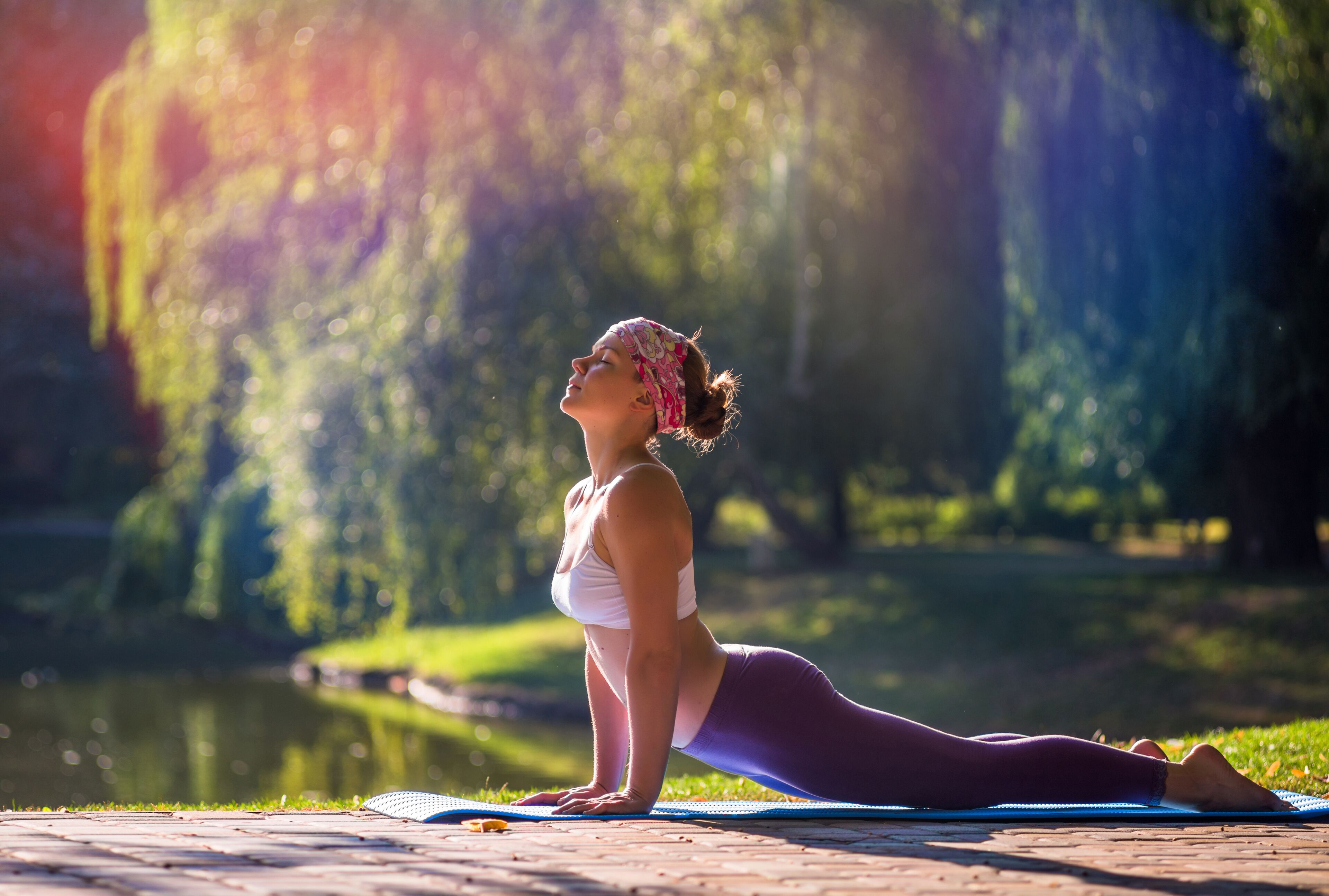 A person performing a yoga pose on a mat in an outdoor setting with a body of water and trees in the background.