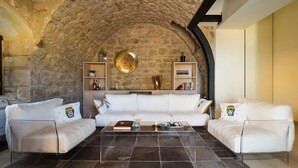 Un salon moderne doté d’un plafond en pierre, de canapés en cuir blanc, d’une table basse en verre et d’étagères intégrées où sont exposés des objets décoratifs.