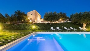 Une piscine rectangulaire à l’eau d’un bleu limpide, entourée d’une pelouse bien entretenue et, au fond, d’un bâtiment en pierre.