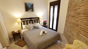 A neatly made bed with a headboard, two bedside lamps, a small table with a basket of flowers, and a chair.