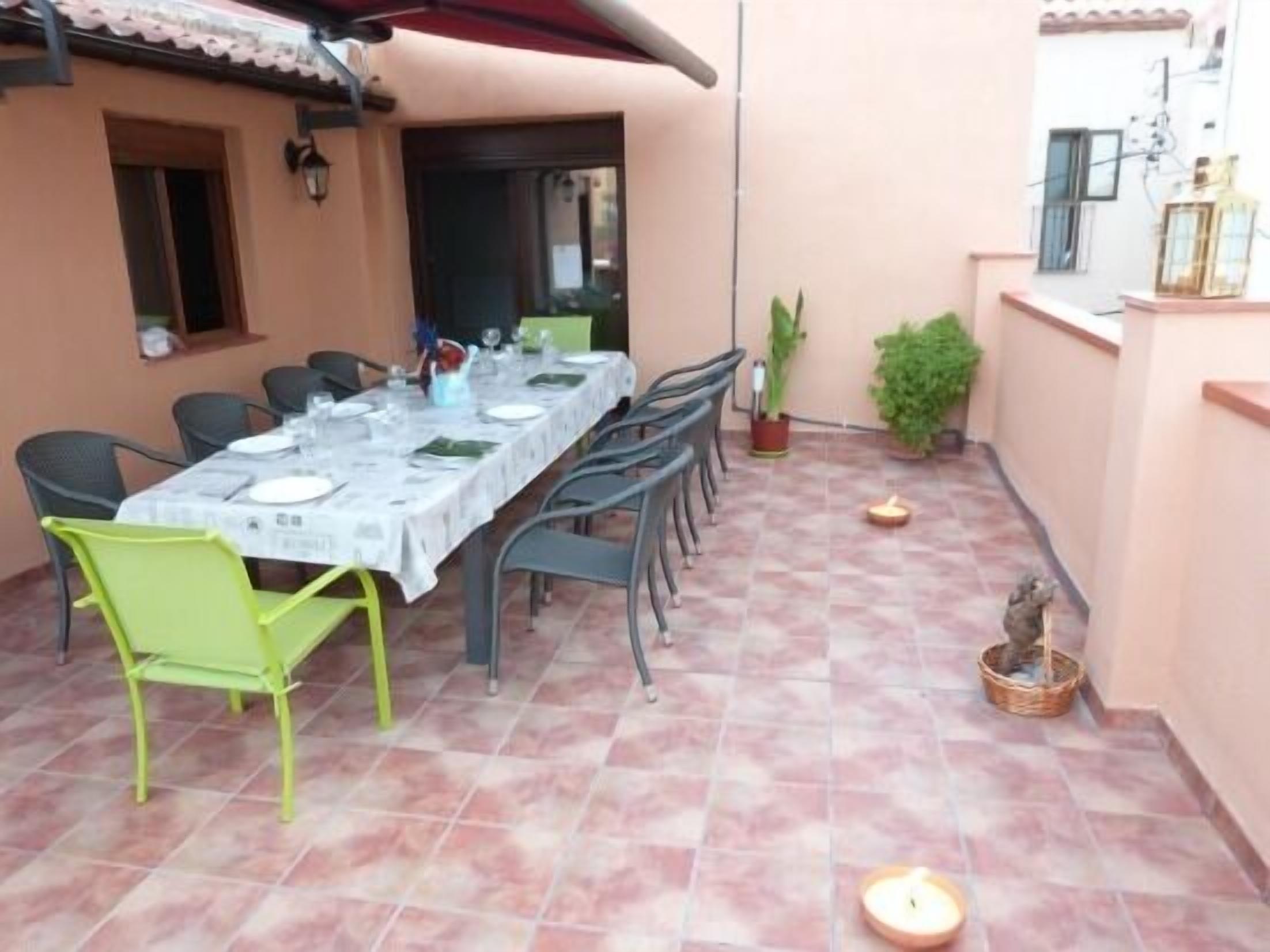 An outdoor dining area with a table set for six, surrounded by chairs, and a tiled floor.