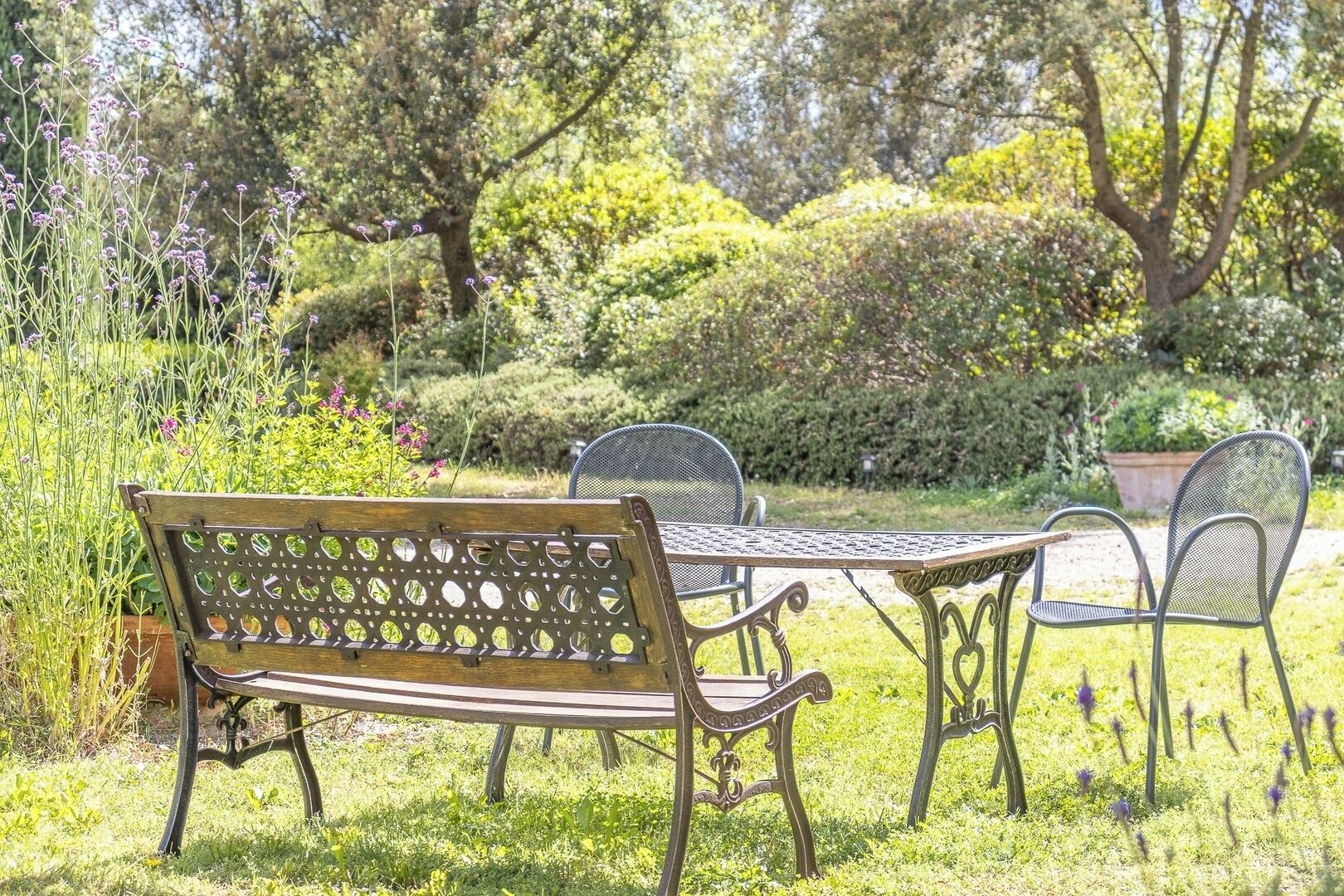 Un jardí amb una cadira de fusta, taula de metall i seients.