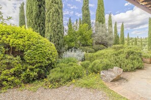 Un jardin avec des haies soigneusement taillées, de grands cyprès et un sentier en pierre.