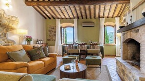 A cozy living room with a stone fireplace, a dining area with a table set for four, and a large window offering a view of the countryside. - Villa Amiata - Tuscan Farmhouse with private pool (Castel del piano)