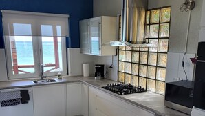 A modern kitchen with a view of the sea, white cabinets, a gas stove, and a coffee maker.