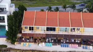 A beachfront hotel with a red-tiled roof, outdoor seating, and a pool.