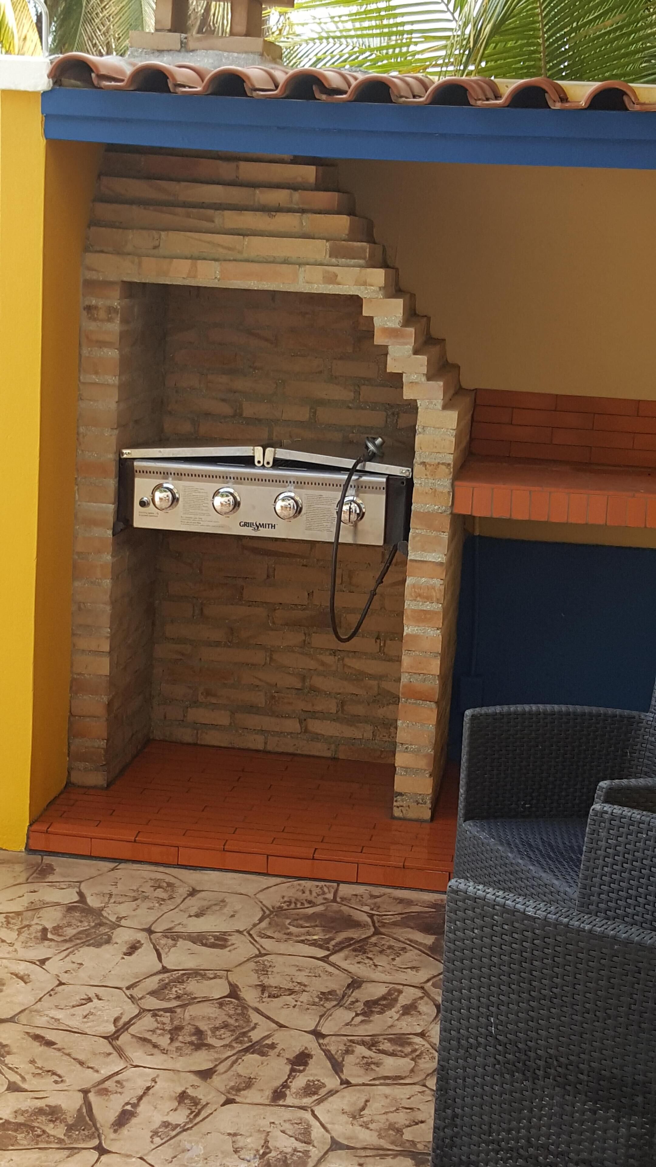 Ulkona sijaitseva grillialue, jossa on Grillsmith-merkkinen grilli, laatoitettu katto ja kuvioitu lattia.