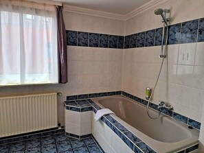 A bathroom with a bathtub, a shower, and a window with curtains.